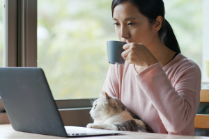 woman sitting at laptop drinking coffee with cat | How to Create Strategies for Content Marketing Based on Pet Trends