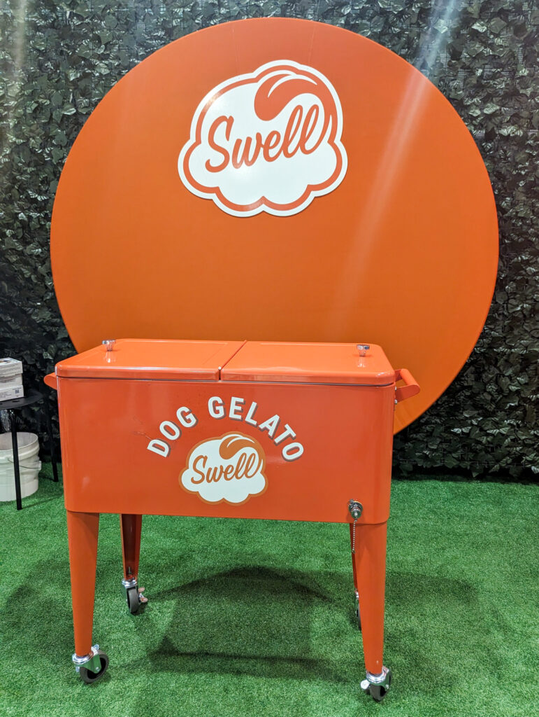 Orange circle backdrop and orange cooler with the Swell logo