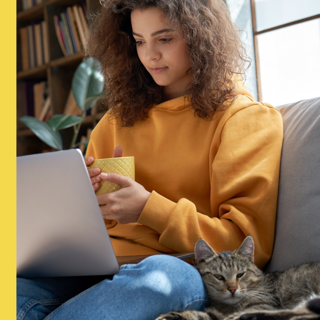 Woman in yellow sweater with cat, computer, and cup of coffee
